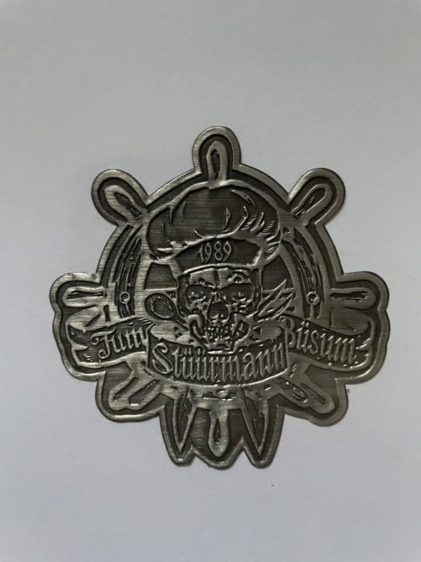 großer, grauer Tum Stüürmann Metall-Aufkleber mit Tum Stüürmann Totenkopf-Koch-Logo vor Steuer