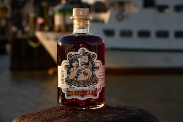 Flasche mit dunkelbraunem Hafenmacker Schoko-Rum vor Schiff im Hafen