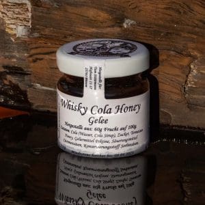 kleines Glas Stüürmann Whisky Cola Honey Aufstrich vor Holzbalken