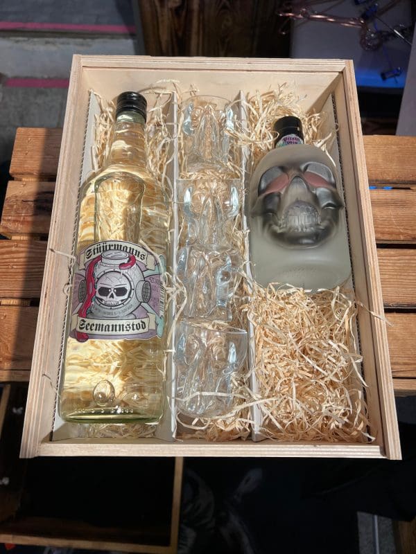 Holzbox mit durchsichtigen Stüürmanns Seemannstod Dragon Gin in der 1 Liter Gastroflasche, vier durchsichtigen Stüürmanns Schädel Schnapsgläser und blassgrüne Stüürmanns Seemannstod Dragon Gin Drachenfrucht-Gin 0,5 Liter Totenkopfflasche
